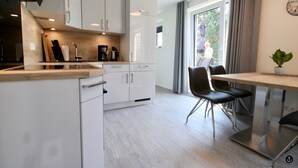 A modern kitchen with white cabinets, a wooden countertop, and a dining area with a table and chairs. - Kapitänshaus 5 (Kellenhusen)