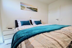Quarto com cama, mesa de cabeceira, porta e um quadro na parede.