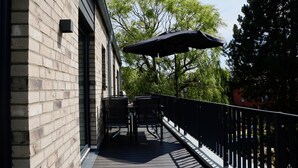 A balcony with a table and chairs, a black umbrella, and a brick building in the background. - Kapitänshaus 5 (Kellenhusen)