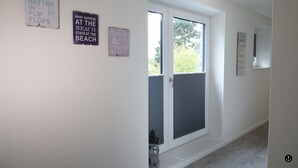 A hallway with a door leading to a balcony, a small table, and three signs on the wall. - Kapitänshaus 5 (Kellenhusen)