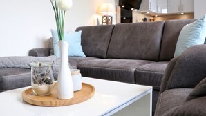 A modern living room with a grey sofa, a white coffee table, and decorative items including a vase with green stems and white spherical objects. - Kapitänshaus 5 (Kellenhusen)