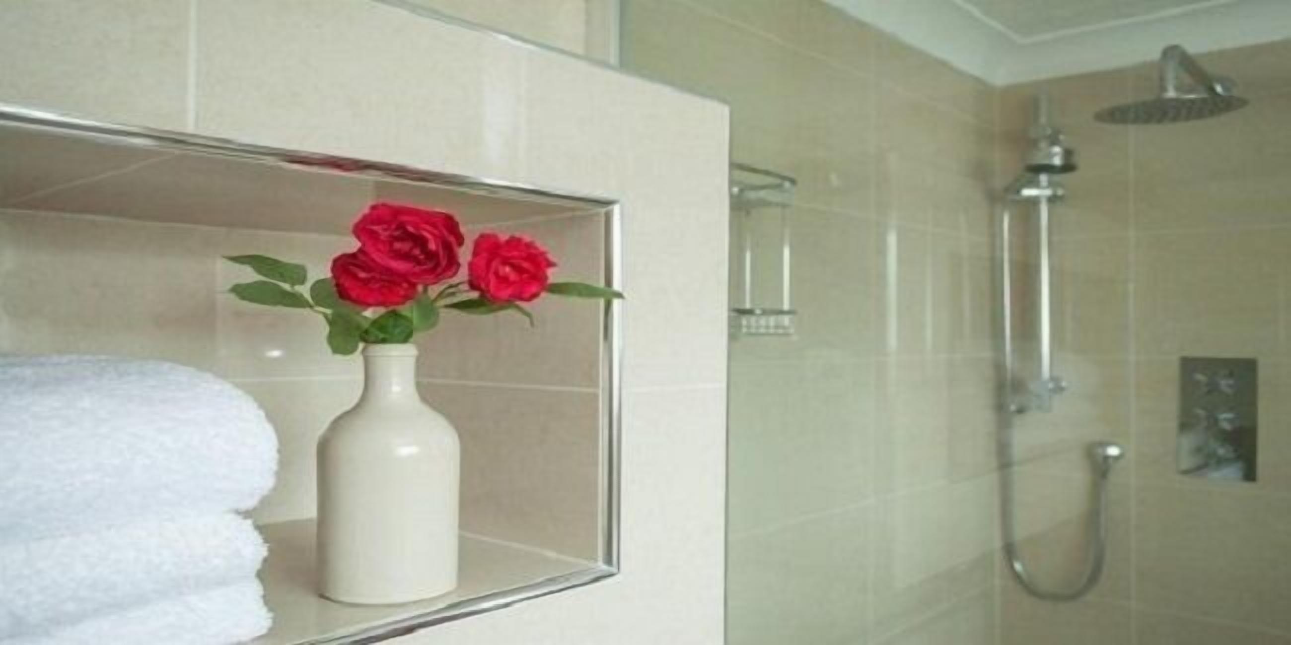 A bathroom with a glass shower enclosure, a white towel, and a vase with red roses.