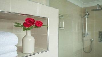A bathroom with a glass shower enclosure, a white towel, and a vase with red roses.