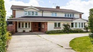 Une maison à deux étages, avec un toit en tuiles, un porche à l’avant et une allée menant à l’entrée.