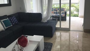 Ein modernes Wohnzimmer mit einem dunkelgrauen Sofa, einem weißen Couchtisch und einer Glasvase. Eine Glastür öffnet sich zu einem überdachten Außenbereich.