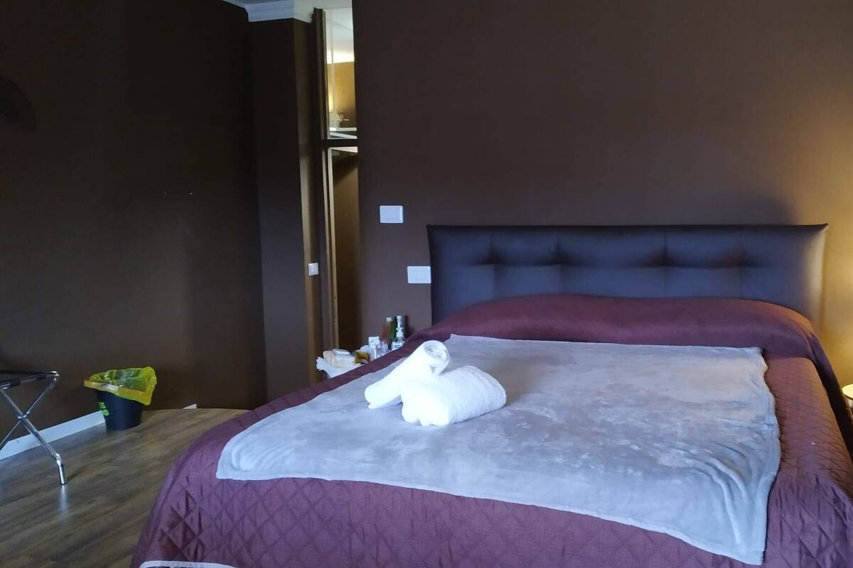 Une chambre d’hôtel avec un grand lit, une table de chevet avec une lampe et une valise posée sur le sol.