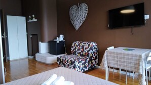 A room with a bed, a sofa, a TV, a table, and a heart-shaped decoration on the wall. - Dolci Emozioni (Bari)
