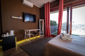 A hotel room with a bed, a desk, a chair, a TV, and a view of the city. - Dolci Emozioni (Bari)