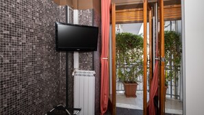 A bathroom with a tiled wall, a flat-screen TV mounted above a white radiator, and a wooden door leading to a balcony with potted plants. - Dolci Emozioni (Bari)