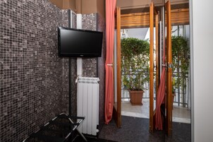 A bathroom with a tiled wall, a flat-screen TV mounted above a white radiator, and a wooden door leading to a balcony with potted plants.