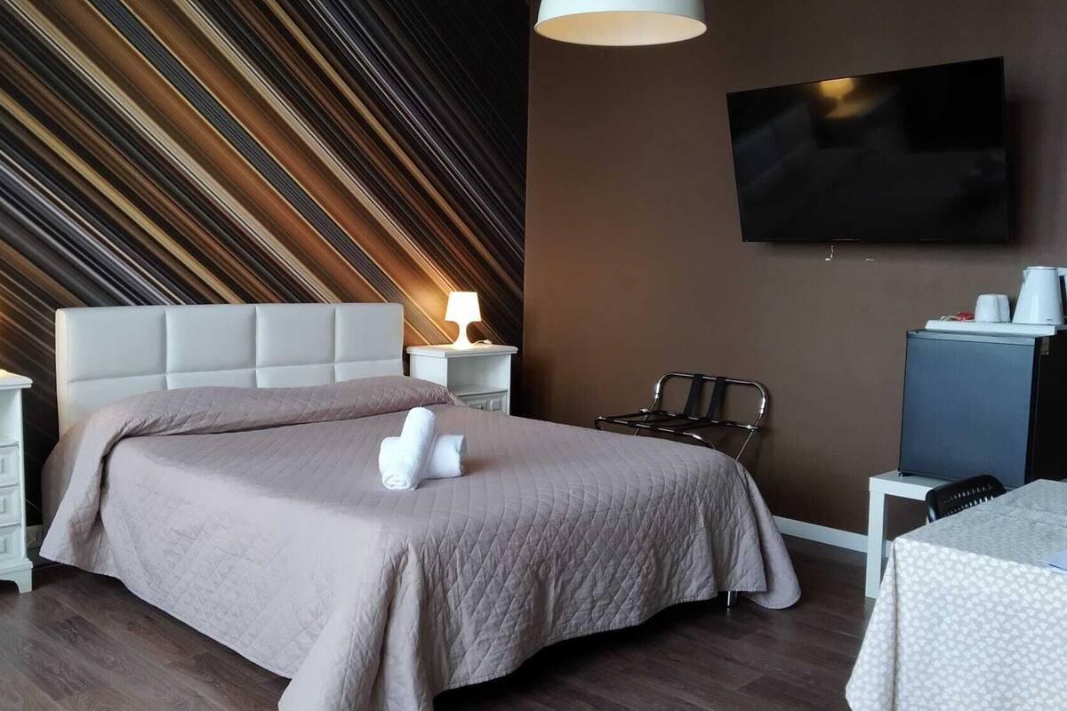 Une chambre d’hôtel avec un grand lit, deux tables de chevet avec des lampes, un téléviseur à écran plat, un bureau avec une chaise et une machine à café.