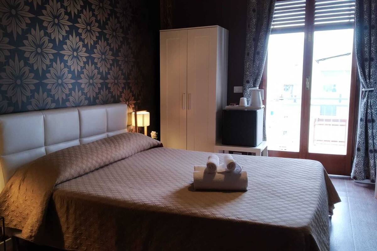 Une chambre à coucher avec un grand lit, une armoire, une table de chevet et une fenêtre avec des rideaux.