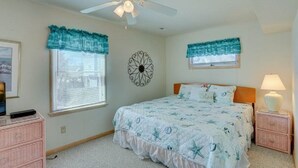 Ein Schlafzimmer mit einem Bett, einem Deckenventilator, einer Wanduhr, einem Fenster mit Jalousien und einem Nachttisch mit Lampe.