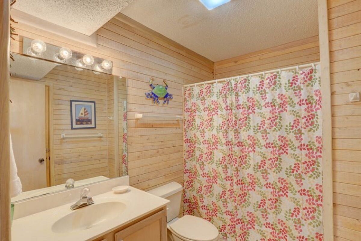 Bany d'una cabana de fusta amb un lavabo de fusta, un rentapel, una tassa i una cortina de dutxa amb un dibuix floral.