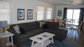 Ein Wohnzimmer mit grauem Sofa, einem weißen Couchtisch und einem Essbereich mit weißen Stühlen und einem Tisch.