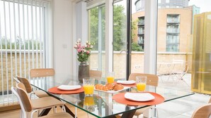 A modern dining area with a glass table, wooden chairs, and a vase of flowers. - Moonside - Stunning Angel Apartments (London)