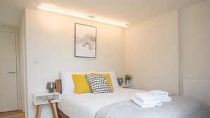 A neatly arranged bedroom with a bed, bedside tables, and a wall-mounted artwork. - Moonside - Stunning Angel Apartments (London)