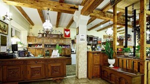 A reception area with wooden furniture, a chandelier, and a stone pillar. - Usługi Noclegowe 17 (Ostrow Mazowiecka)