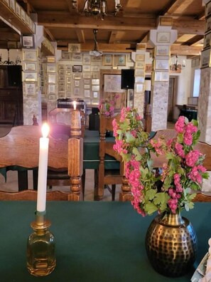 Una habitación con techo de madera, cuadros en las paredes, una mesa con una vela y un jarrón con flores.