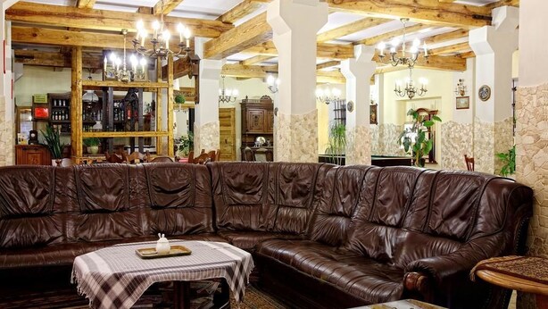 A cozy living room with a brown leather sofa, a small table with a checkered tablecloth, and a chandelier. - Usługi Noclegowe 17 (Ostrow Mazowiecka)