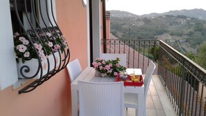 A balcony with a white table and chairs, a flower arrangement, and a view of a hilly landscape. - B&B Villa Milena (Ariano Irpino)