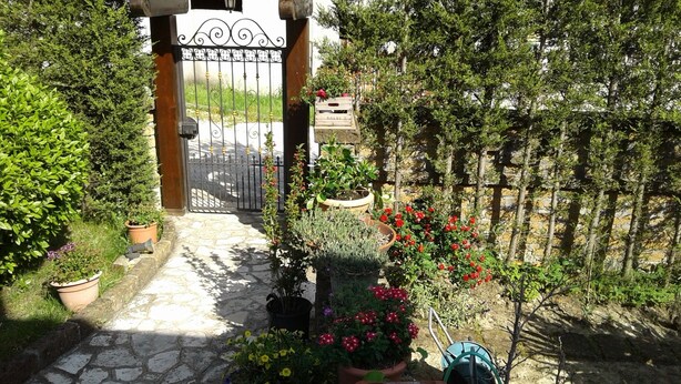 A stone-paved entrance with a wrought iron gate, surrounded by potted plants and flowering shrubs. - B&B Villa Milena (Ariano Irpino)