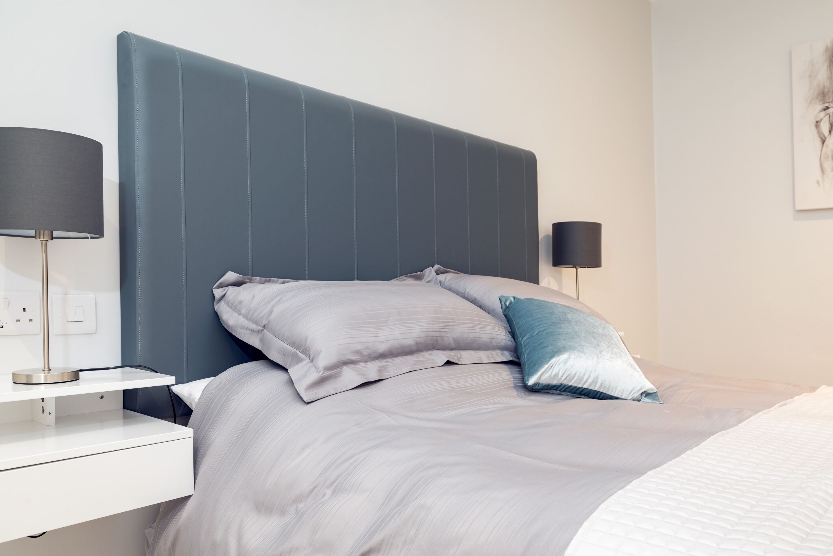 A modern bedroom with a large bed, two bedside tables, and a wall-mounted lamp.