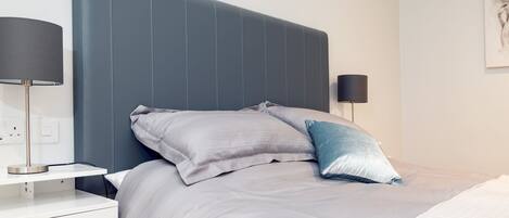 A modern bedroom with a large bed, two bedside tables, and a wall-mounted lamp.