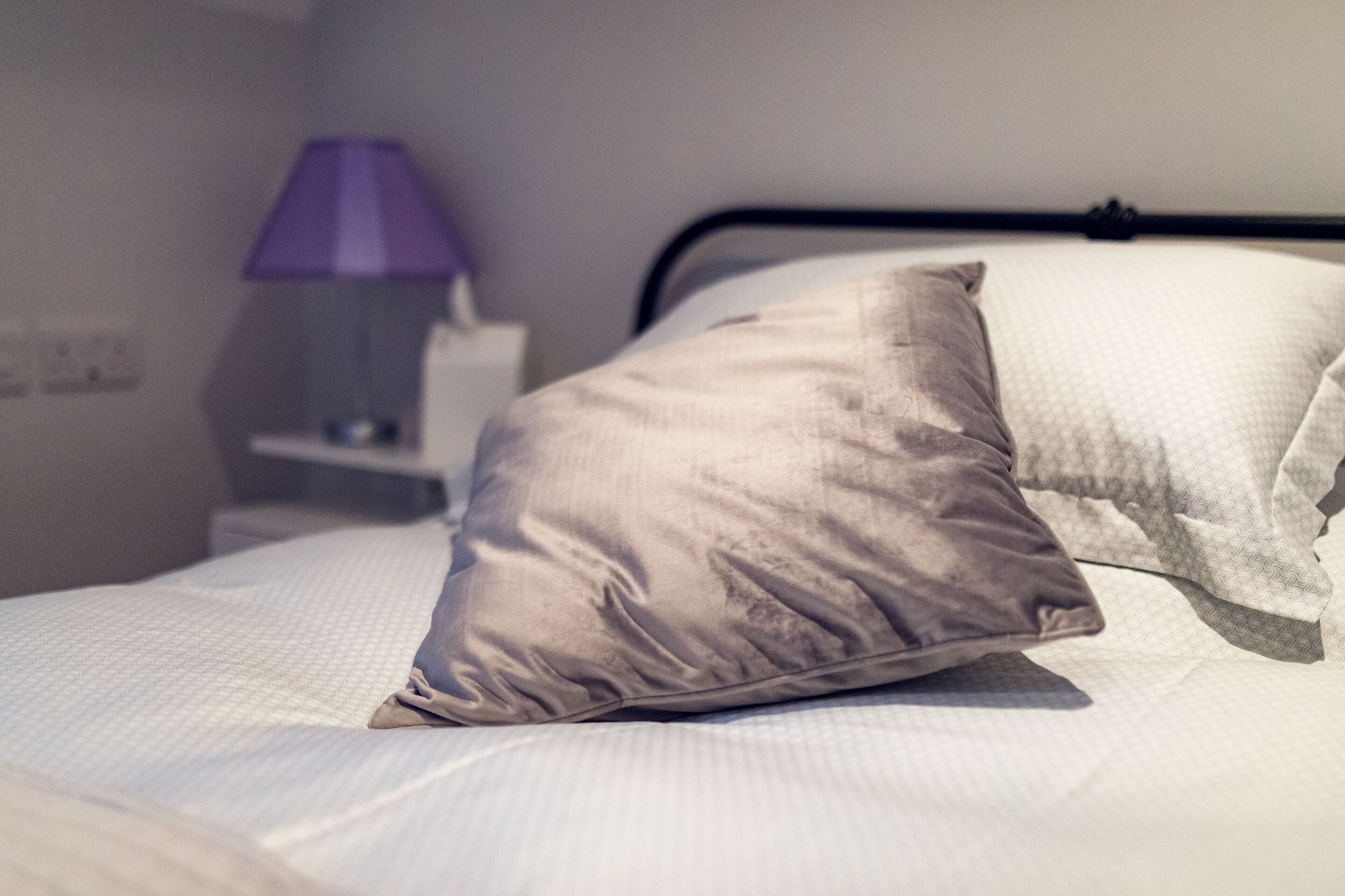 A neatly made bed with a single pillow and a lamp in the background.