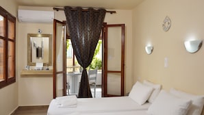 A bedroom with two beds, a wooden floor, a window with curtains, a mirror, and a wall-mounted light fixture. - Urban Studios Manos (Chania)