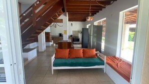 Ein modernes Interieur mit einem weißen Sofa, orangefarbenen Kissen, einer Treppe und einer Küchenzeile.