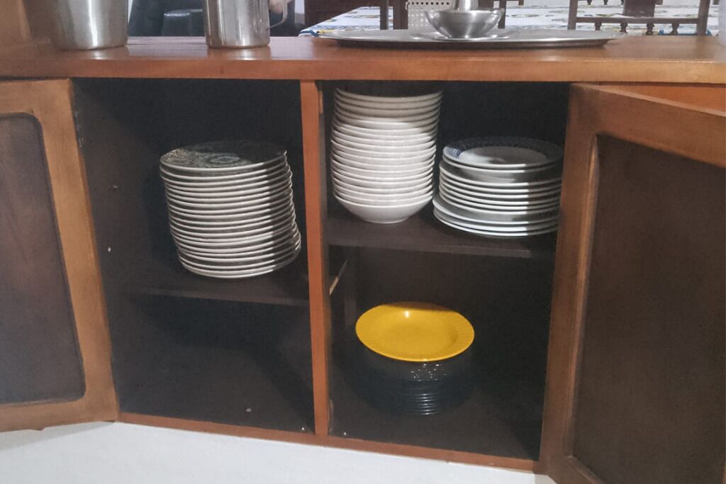 A kitchen cabinet with multiple shelves holding stacks of plates and a yellow bowl.