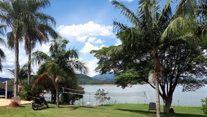 Eine Rasenfläche mit Volleyballnetz, Palmen und Blick auf See und Berge.