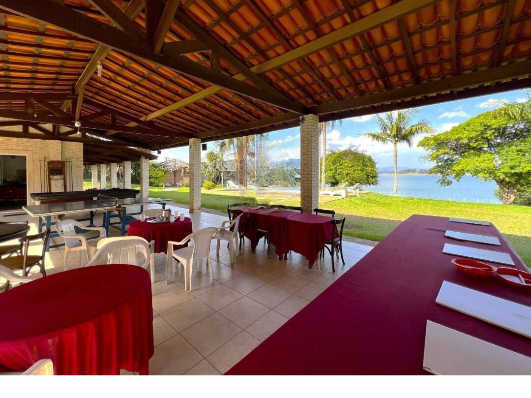 An outdoor dining area with tables and chairs, a covered roof, and a view of the water and greenery.