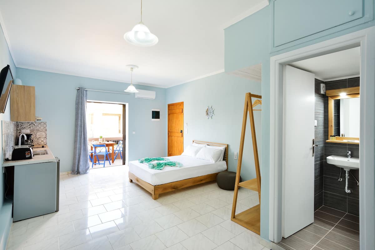 A bedroom with a bed, a desk, a chair, a mirror, and a bathroom with a sink and shower.