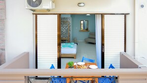 A balcony with a table set for two, a bed, and a sofa in the adjacent room. - Katerina Apartments 1 (Chania)