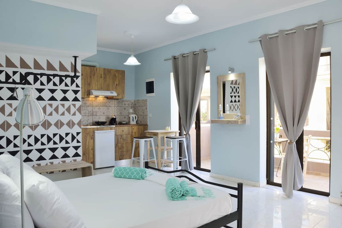 A modern bedroom with a bed, a desk, and a kitchenette.