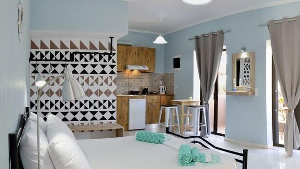 A modern hotel room with a bed, a desk, a chair, a small kitchen area, and a balcony. - Katerina Apartments 1 (Chania)