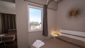 A hotel room with a bed, a window with curtains, a chair, a small table, and a wall clock. - CconfortHotels R&B Cavour (Bari)