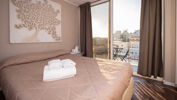 A hotel room with a large bed, a view of the city through a balcony, and a decorative tree artwork on the wall. - CconfortHotels R&B Cavour (Bari)