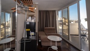 A modern hotel room with a sofa, two small tables, a coffee machine, and a view of the city through large windows. - CconfortHotels R&B Cavour (Bari)