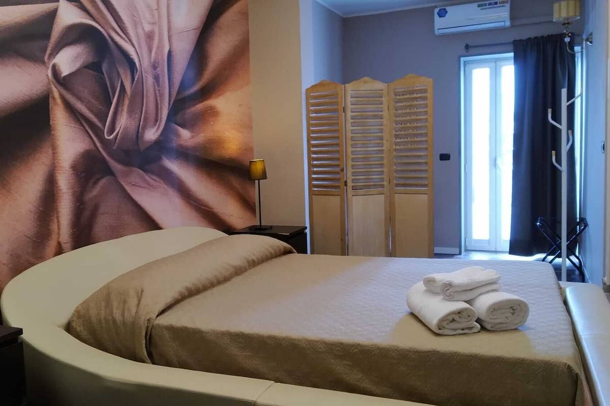 Ett hotellrum med en stor säng, en väggmålning, en sänglampa, en garderob och ett fönster med gardiner.