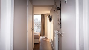 A narrow hallway with a bed at the end, a radiator on the right, and a view of buildings outside. - CconfortHotels R&B Cavour (Bari)