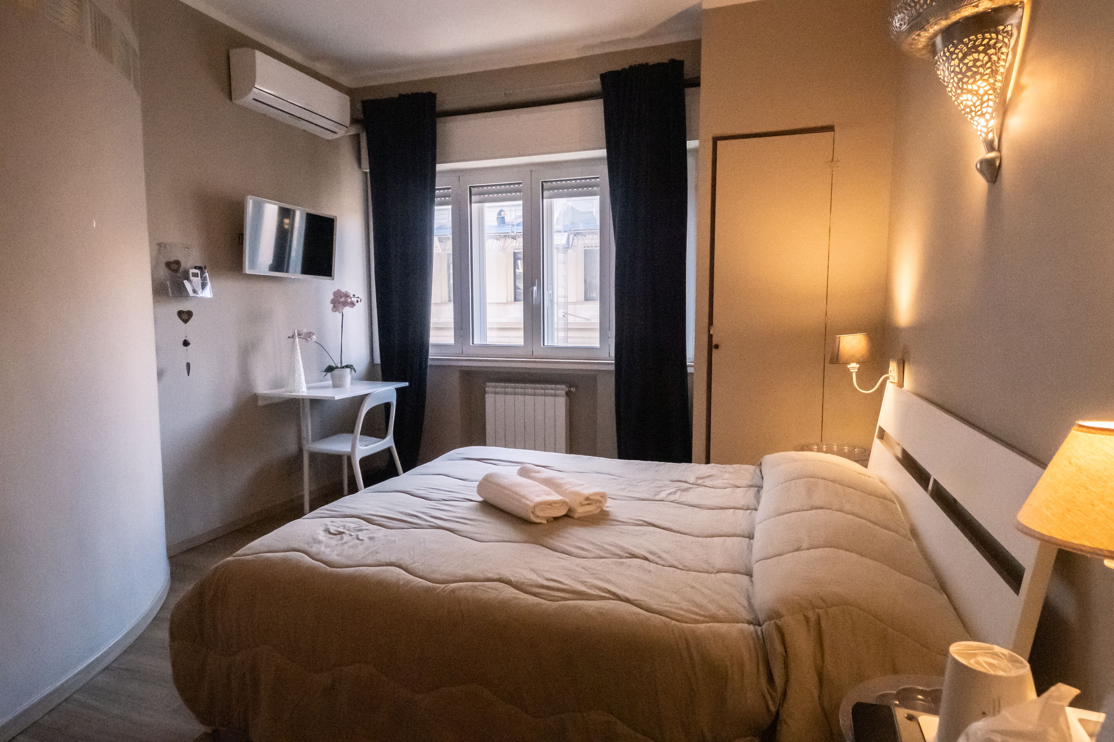 A hotel room with a bed, a desk, a chair, a TV, and a window with curtains.