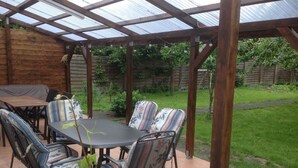 A covered patio with a table and chairs, surrounded by a wooden fence and greenery. - Altstadt-Garni (Bad Windsheim)