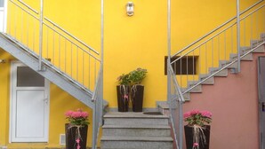 A staircase leading to a building with a yellow exterior and a white door. There are two potted plants with pink flowers at the base of the stairs. - Altstadt-Garni (Bad Windsheim)