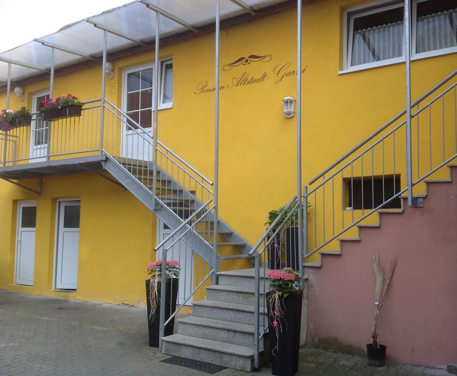 A yellow building with a staircase and flower planters.