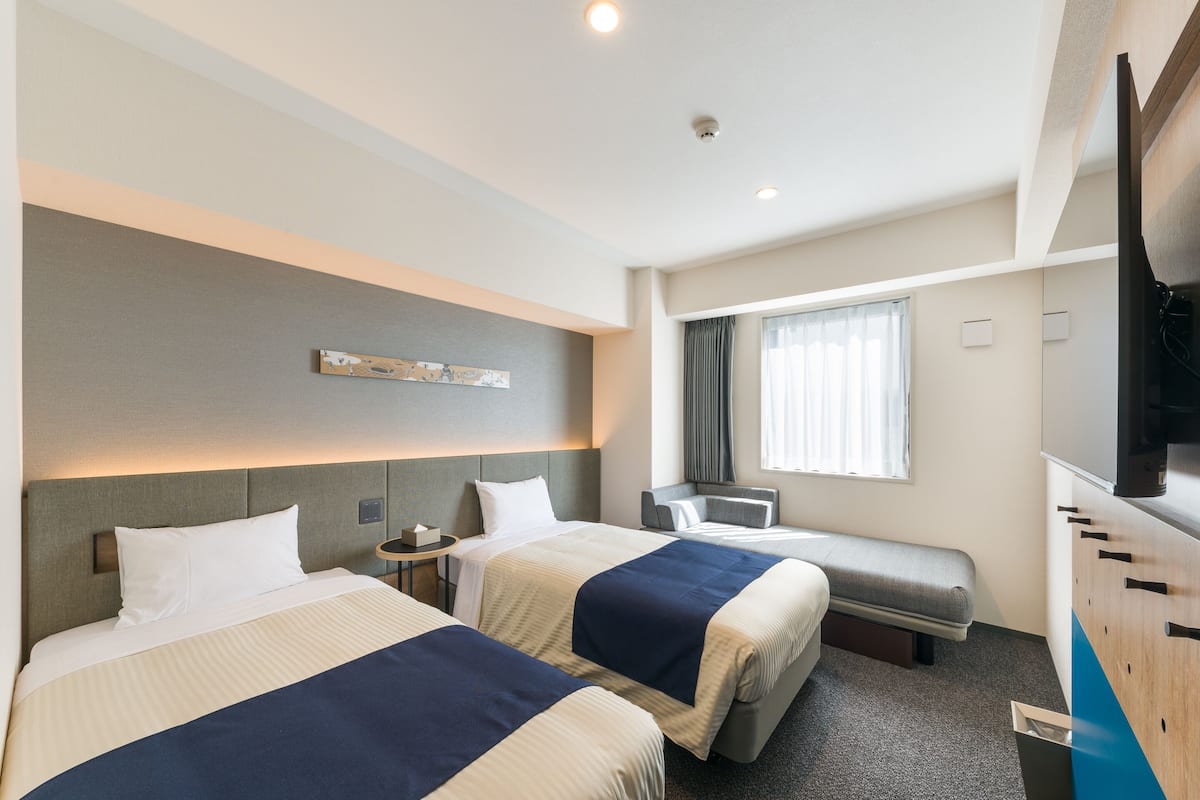 A hotel room with two beds, a TV, a desk, and a window with curtains.
