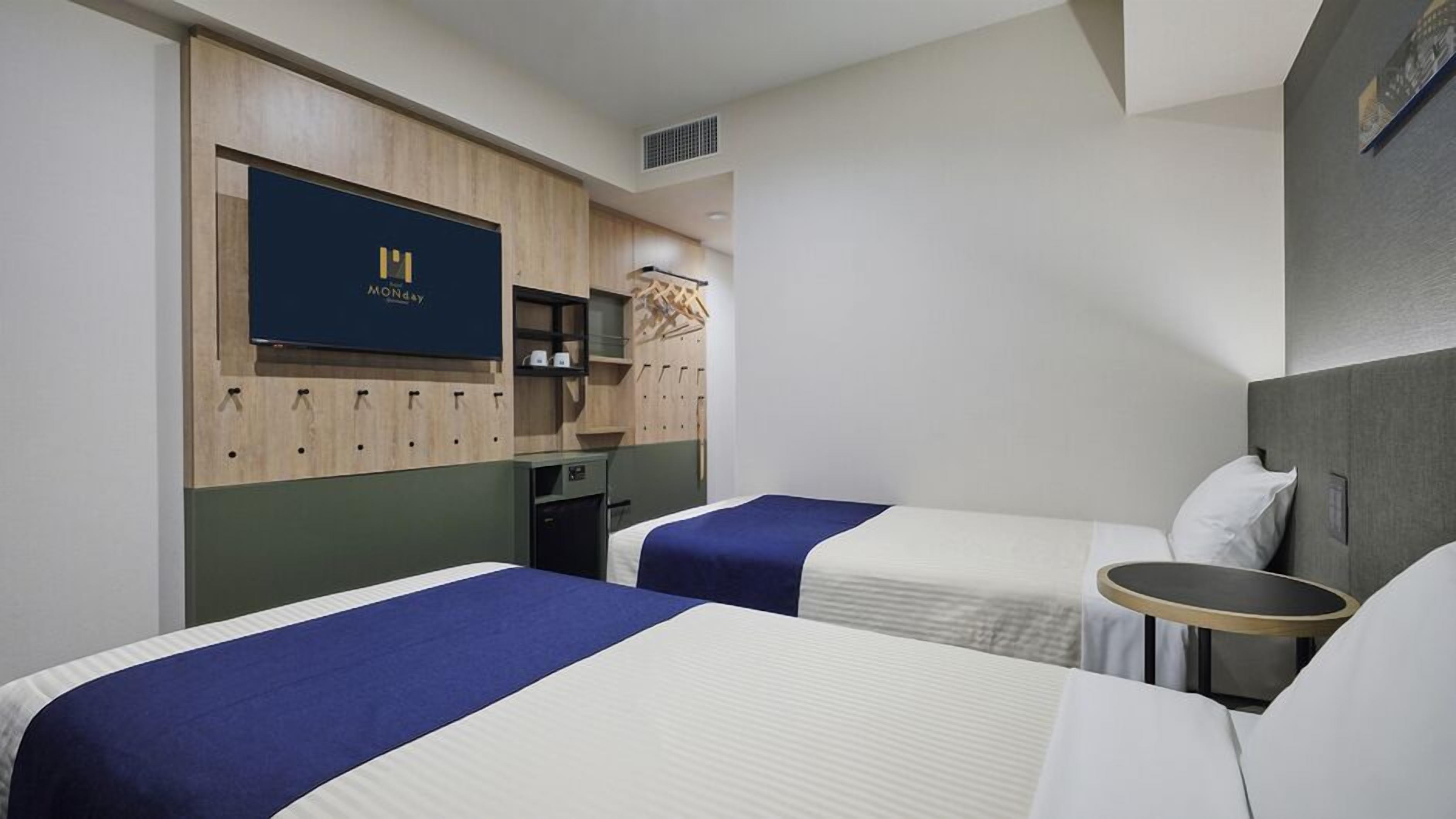 A hotel room with two beds, a TV mounted on the wall, a desk, and a wardrobe.