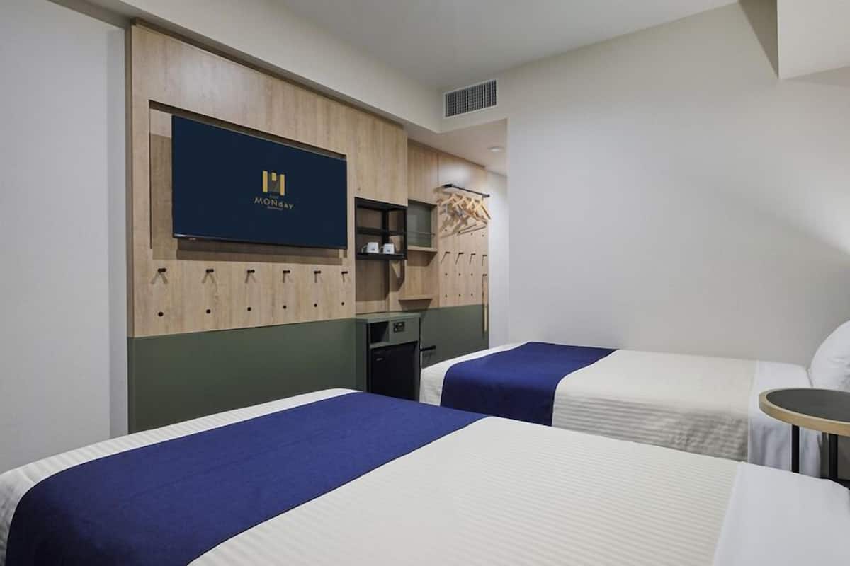 A hotel room with two beds, a TV mounted on the wall, a desk, and a wardrobe.